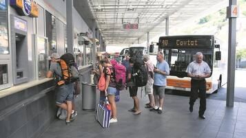 A bus station with a digital clock displaying 10:16, a bus labeled 'Cavist', and people waiting.