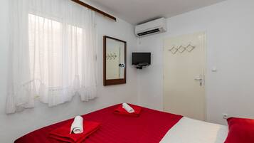 Habitación de hotel con cama, televisor montado en la pared, unidad de aire acondicionado y puerta con espejo y detalles decorativos.