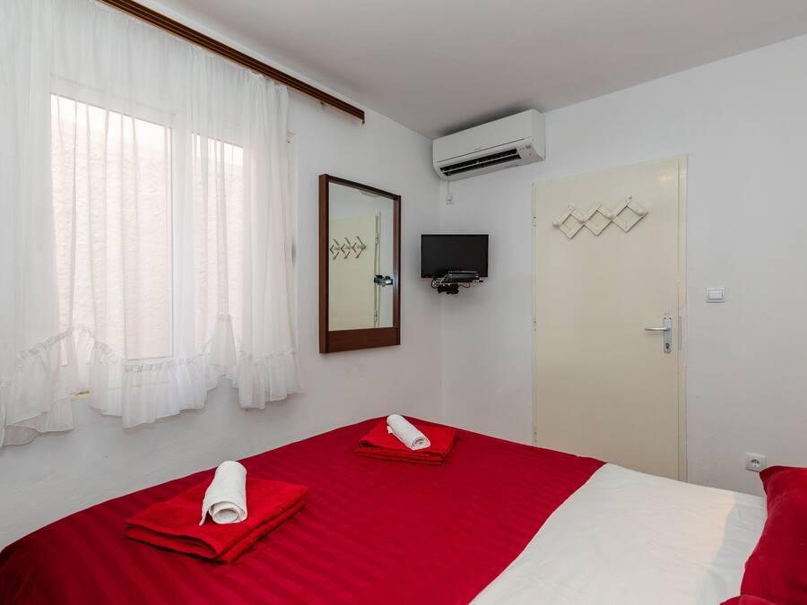 Habitación de hotel con cama, televisor montado en la pared, unidad de aire acondicionado y puerta con espejo y detalles decorativos.
