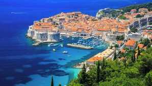 A coastal town with historic architecture, a harbor with boats, and a prominent fortification. - Rooms Edna (Dubrovnik)