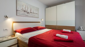 A neatly made bed with red bedding, a wooden headboard, and a painting of sailboats on the wall. - Rooms Edna (Dubrovnik)