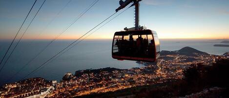 A cable car with passengers, a coastal cityscape, and a mountain in the background.