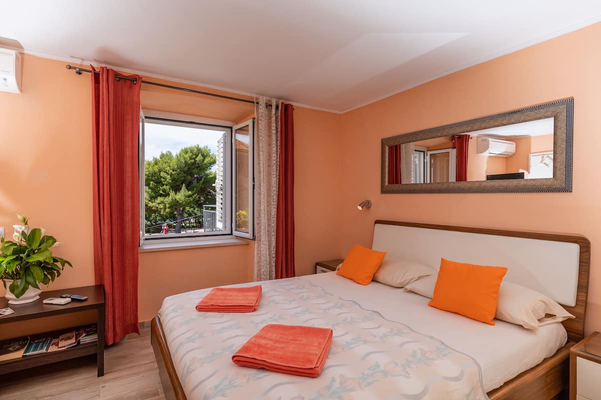 Un dormitorio con cama, dos almohadas, una mesita de noche, un espejo y una ventana con cortinas.