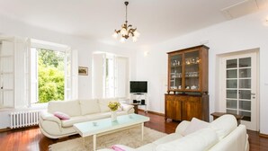Una sala de estar con un sofá blanco, una mesa de centro de vidrio, un mueble de madera con puertas de cristal y un televisor.