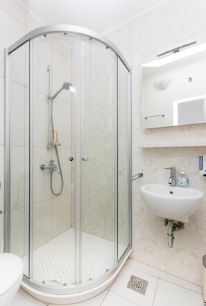 Un baño moderno con ducha de vidrio, un lavabo blanco y un espejo sobre el lavabo.