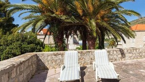 Dos sillones de descanso en una terraza de piedra, con una palmera y un muro de piedra al fondo.