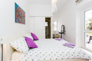 Un dormitorio con una cama, una ventana, una puerta y un cuadro en la pared.