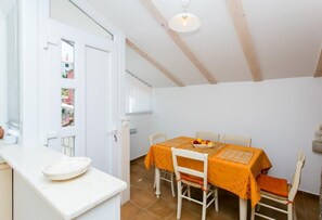 Un comedor con una mesa dispuesta para dos personas, una encimera blanca con un tazón y vistas al exterior a través de una puerta.
