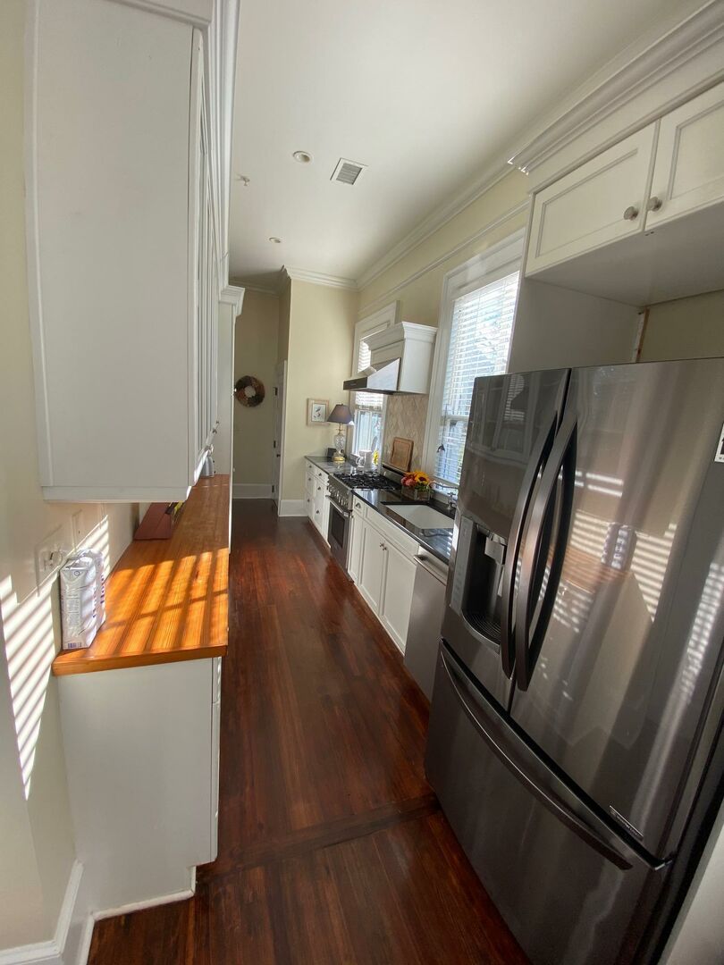 A kitchen with white cabinets, a stainless steel refrigerator, and a wooden countertop.