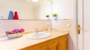 A bathroom with a white sink, wooden vanity, and a mirror above the sink. There are two towels hanging on the wall and a small plant on the vanity. - Villa Marina (Campos)