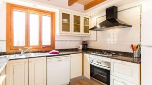 A kitchen with white cabinets, a stainless steel sink, a stove, and a black range hood. - Villa Marina (Campos)