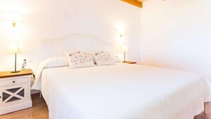 A white bedroom with a wooden ceiling, a bed with floral pillows, and bedside lamps. - Villa Marina (Campos)