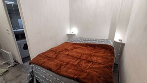 A bedroom with a bed, a washing machine, and a small bathroom visible through an open door. - Renovated Studio - South Balcony - 6 Pers - Ski/Hike (Saint-Michel-de-Chaillol)