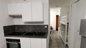 A compact kitchen with white cabinets, a black countertop, and a built-in oven. - Renovated Studio - South Balcony - 6 Pers - Ski/Hike (Saint-Michel-de-Chaillol)