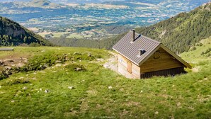 A wooden cabin with a sloped roof, surrounded by lush green hills and a panoramic view of distant mountains. - Renovated Studio - South Balcony - 6 Pers - Ski/Hike (Saint-Michel-de-Chaillol)