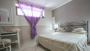 A bedroom with a bed, a desk, and a window with purple curtains. - La Fenice (Boscoreale)