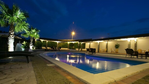 Une piscine agrémentée d’une pergola et de chaises, entourée de palmiers et surplombée par le ciel nocturne.