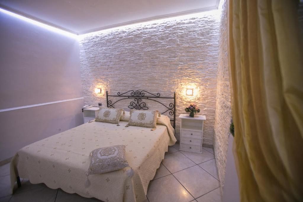A bedroom with a stone wall, a bed with a patterned bedspread, two bedside tables with lamps, and a curtain on the right.