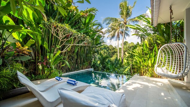 A poolside area with lounge chairs, a hanging chair, and lush tropical vegetation. - Romantic Jungle Villa, 1 BR, Ubud With Staff (Ubud)