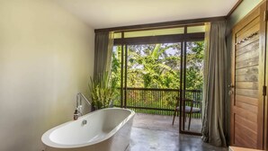Ein Badezimmer mit freistehender Badewanne, einer Holztür und Blick auf einen üppigen Garten durch eine Schiebetür.