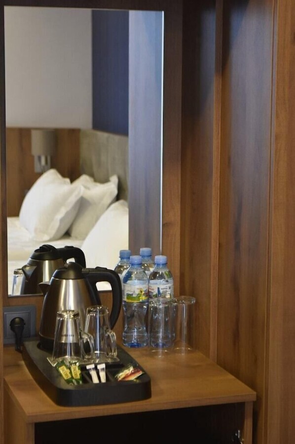 Habitación de hotel con un escritorio de madera, una tetera, una bandeja con condimentos y agua embotellada.