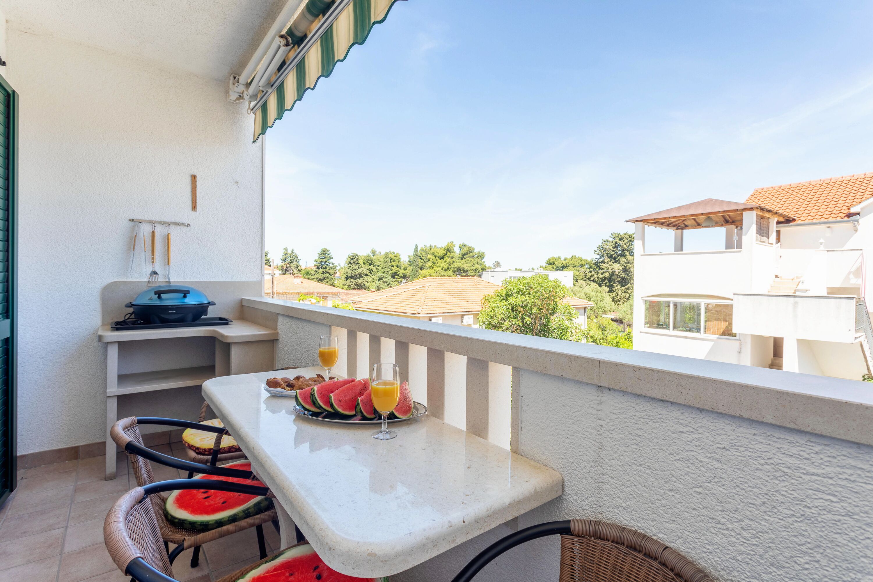 Ein Balkon mit Frühstückstisch, mit Wassermelonenstücken und Orangensaft, mit Blick auf eine Wohngegend.