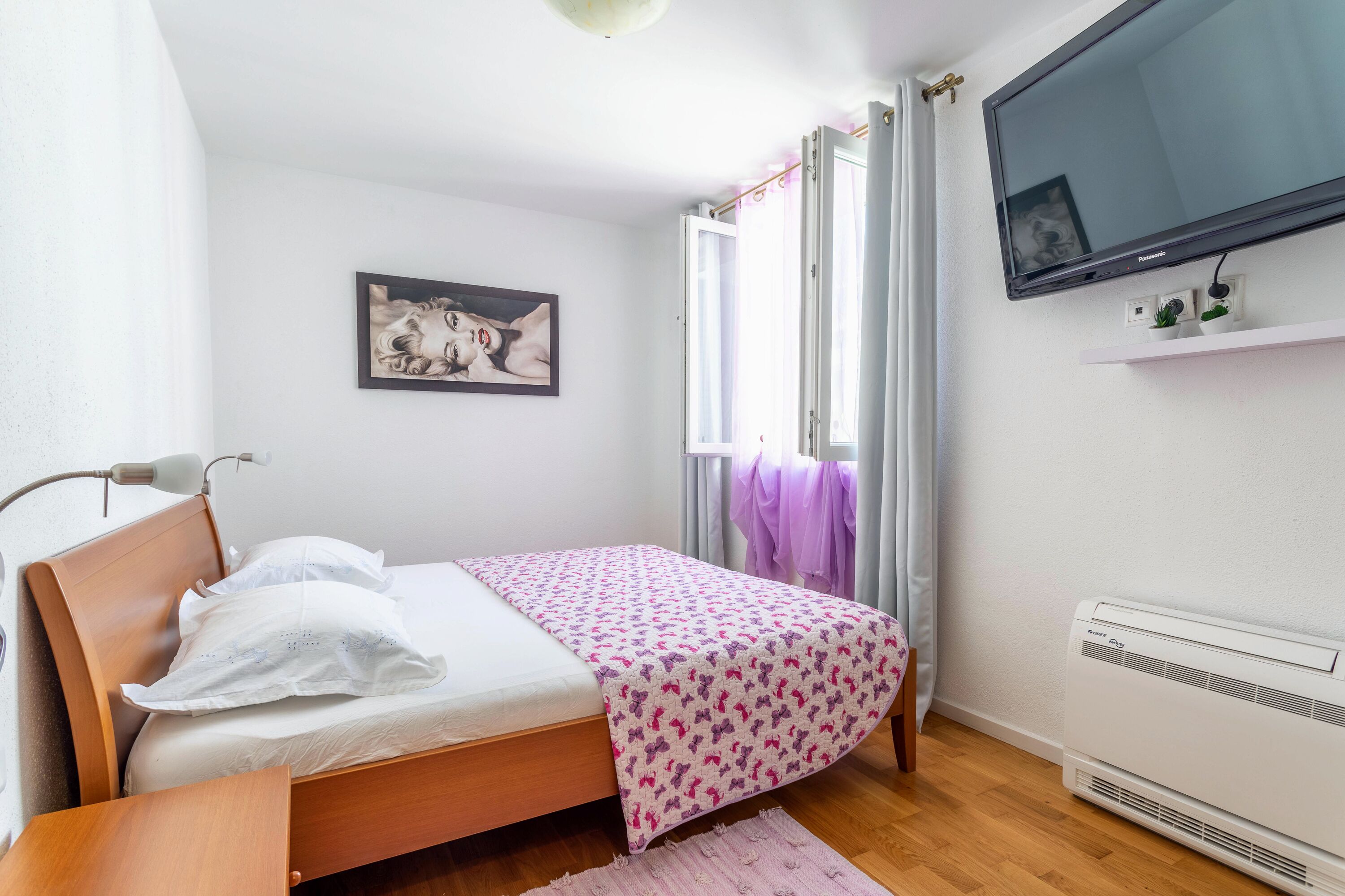 Une chambre à coucher avec un lit, une télévision, un radiateur et une fenêtre avec des rideaux.
