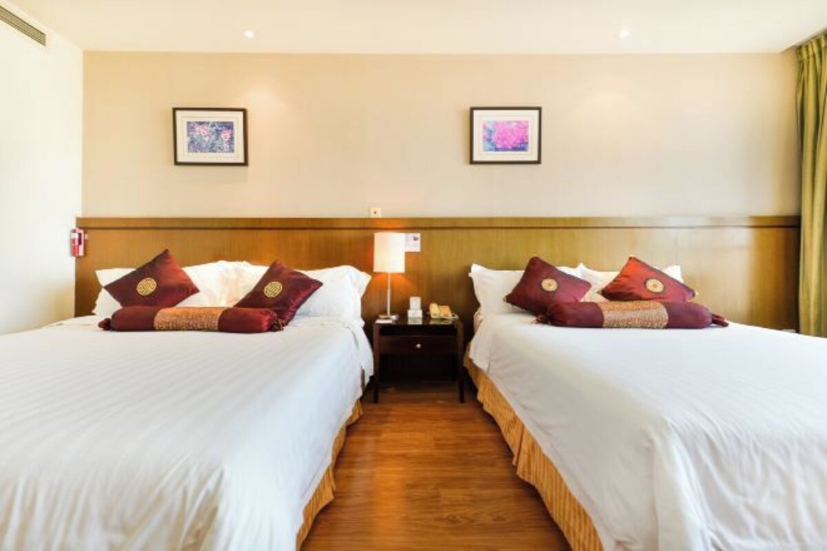 A hotel room with two beds, a nightstand, a lamp, and two framed pictures on the wall.