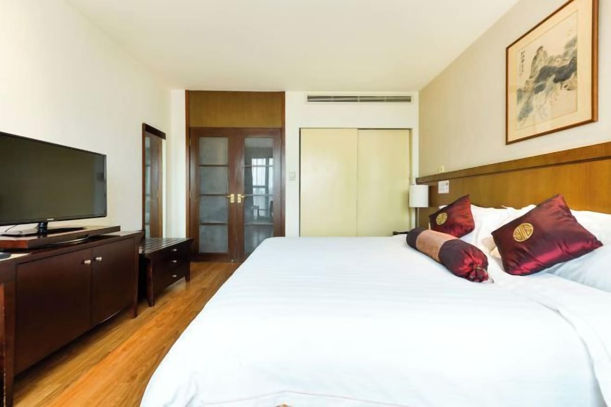 A hotel room with a bed, a TV on a wooden cabinet, a wardrobe, and a door leading to a bathroom.