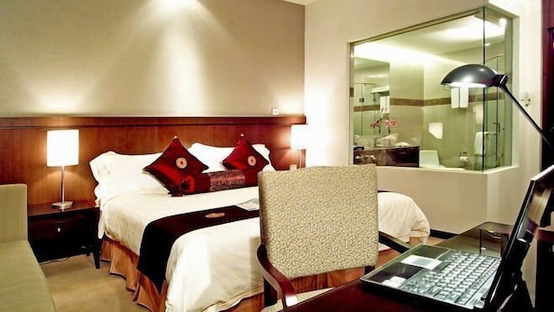 Ein Hotelzimmer mit Bett, Schreibtisch mit Laptop, Stuhl, Nachttisch und Spiegel.