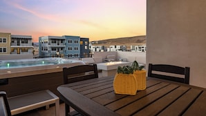 A terrace with a hot tub, seating area, and a view of buildings and hills. - Attitude Adjustment Retreat: Desert Color Lagoon + Beaches (St. George)