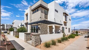 A modern two-story house with a stone facade, a covered patio, and a clear view of the surrounding landscape. - Attitude Adjustment Retreat: Desert Color Lagoon + Beaches (St. George)