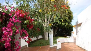 A courtyard with a tiled floor, a white wall, and a tree with pink flowers. - Caniço Bay Apartments (Caniço)