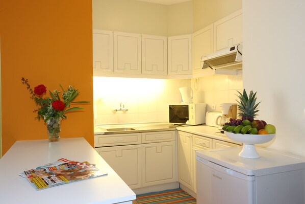A compact kitchen with white cabinets, a microwave, a coffee maker, and a fruit bowl on the counter. - Caniço Bay Apartments (Caniço)