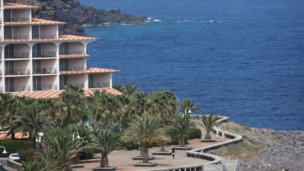 A multi-story hotel with balconies overlooking a rocky coastline and the sea. - Caniço Bay Apartments (Caniço)