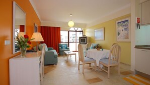 A hotel room with a dining area, a TV, and a window with curtains. - Caniço Bay Apartments (Caniço)