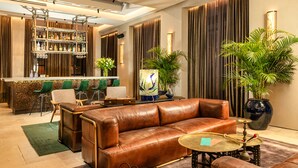Un espacio lounge moderno con sofás de cuero, una barra con estantes llenos de botellas y plantas decorativas.