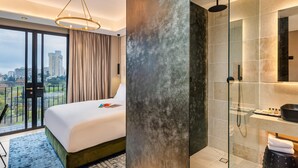 Una habitación de hotel moderna con una cama grande, un box de ducha con paredes de vidrio y vistas a la ciudad a través de las puertas del balcón.