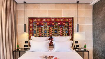 A hotel room with a large bed, two bedside tables, a decorative tapestry on the headboard, and a curtain on the left side.