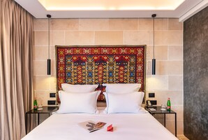 Una habitación de hotel con una cama grande, dos mesitas de noche, un tapiz decorativo en la cabecera y una cortina a la izquierda.
