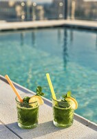 Dos vasos de bebida verde con rodajas de limón y hojas de menta, sobre un borde de piscina.