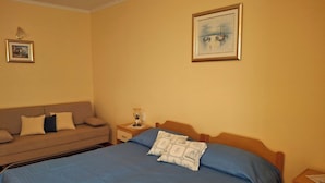 Un dormitorio con cama, mesita de noche, lámpara, un cuadro en la pared y un sofá.