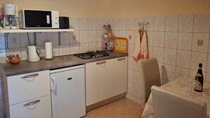 Cocina compacta equipada con microondas, tostadora, hervidor y un refrigerador pequeño. Se observa un reloj en la pared y una mesa con una botella y vasos.