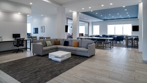 Een ruime werkruimte met een grijze modulaire bank, een witte salontafel en een donker vloerkleed.