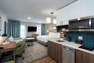 Habitación de hotel con cama, escritorio, silla, televisor, microondas, cafetera y lavavajillas.