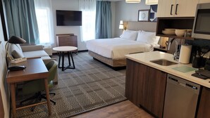 A hotel room with a bed, a desk with a chair, a small table, a sofa, a kitchen area with a sink and a dishwasher, and a flat-screen TV mounted on the wall. - Staybridge Suites Louisville Expo Center by IHG (Louisville)