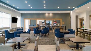 A modern dining area with tables and chairs, a bar, and a flat-screen TV on the wall.