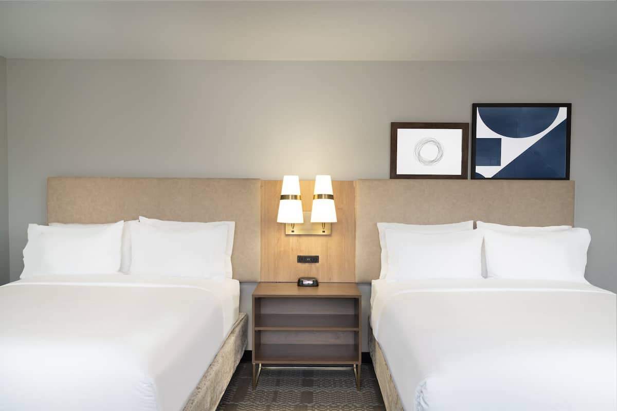 Una habitación de hotel con dos camas, una mesita de noche con lámparas y dos cuadros en la pared.