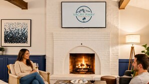 A living room with a fireplace, a framed logo on the wall, and a coffee table with decorative items. - 9BR Riverfront Estate | Pool, Theater, Game Room, on Shenandoah River (Shenandoah)