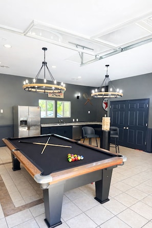 Une table de billard avec des billes, un réfrigérateur et un coin cuisine avec des chaises et une table.